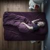 Graumellierter, bärtiger Mann schläft auf der Seite liegend in lila Bettwäsche, von oben fotografiert