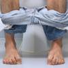 Mann mit herunter gelassener Hose auf Toilette
