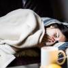 Frau mit Grippe liegt im Bett, das Taschentuch vor der Nase