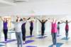 4 Frauen stehen in Sportstudio auf Yogamatten und strecken ihre Arme seitlich nach hinten
