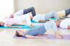 Yoga-Gruppe in Pastell macht Übungen auf dem Rücken liegend 