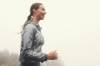 Junge Frau joggt im Nebel und trägt ein graues Oberteil