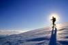 Mann geht in Schneeschuhen im Gegenlicht einen verschneiten Berg hinunter