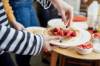 Person in schwarzgeringeltem, langärmeligen T-Shirt bestreut sich am Frühstücksbuffet einen Pancake auf Teller mit Heidelbeeren und geschnittenen Erdbeeren