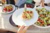 An sommerlicher Tafel wird ein mediterraner Nudelsalat auf einen Teller gegeben