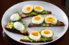 Weisser Teller mit diagonal geschnittenen und mit Avocado und gekochten Eier belegten Vollkornbrotscheiben