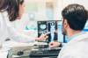 Arzt lässt sich am Schreibtisch sitzend von einer Kollegin auf seinem Monitor Röntgen-Bilder erklären