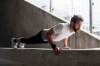 Hipster mit Vollbart, frisch gescheitelt und gegelt, macht Liegestütze auf Beton-Balustrade