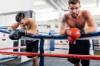 Zwei bärtige und gescheitelte Boxer stützen sich im Boxring am Seil ab und schauen abgekämpft in die Kamera