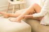 Frau mit blanken Beinen sitzt auf Wohnzimmerpolster und hält sich die Wade ihres angewinkelten linken Beins
