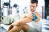 Junger Mann hält sich in einem Fitnessstudio mit schmerzverzerrtem Gesicht ein Coolpack auf seinen rechten Arm